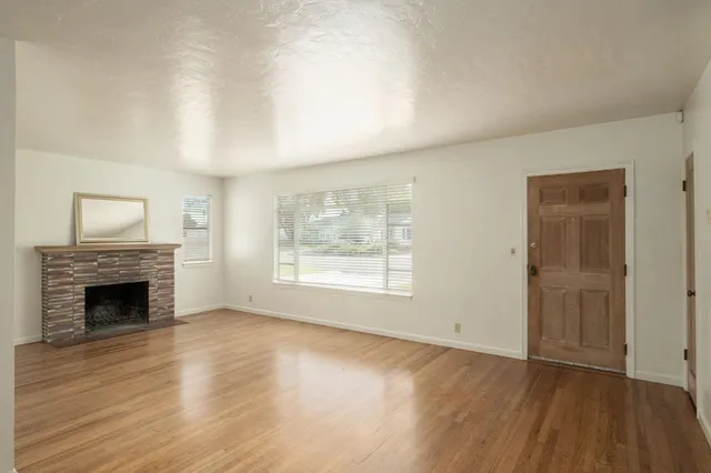 an empty room with wooden floor fireplace and windows
