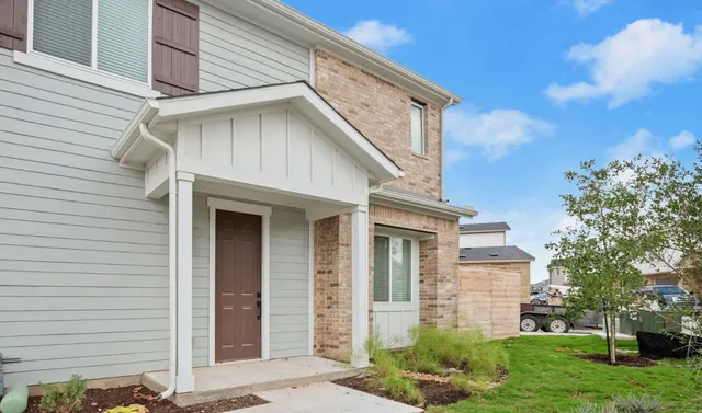 a white house with a small yard plants and a large tree
