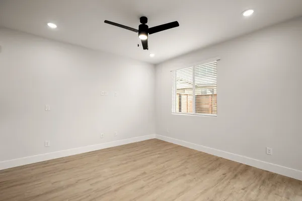 an empty room with wooden floor ceiling fan and windows