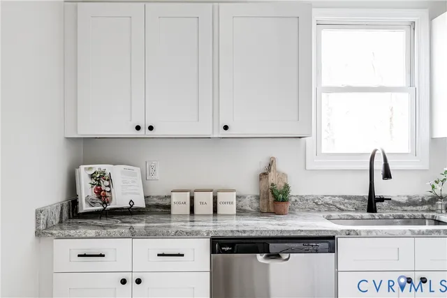 a kitchen with granite countertop a sink white cabinets and a window