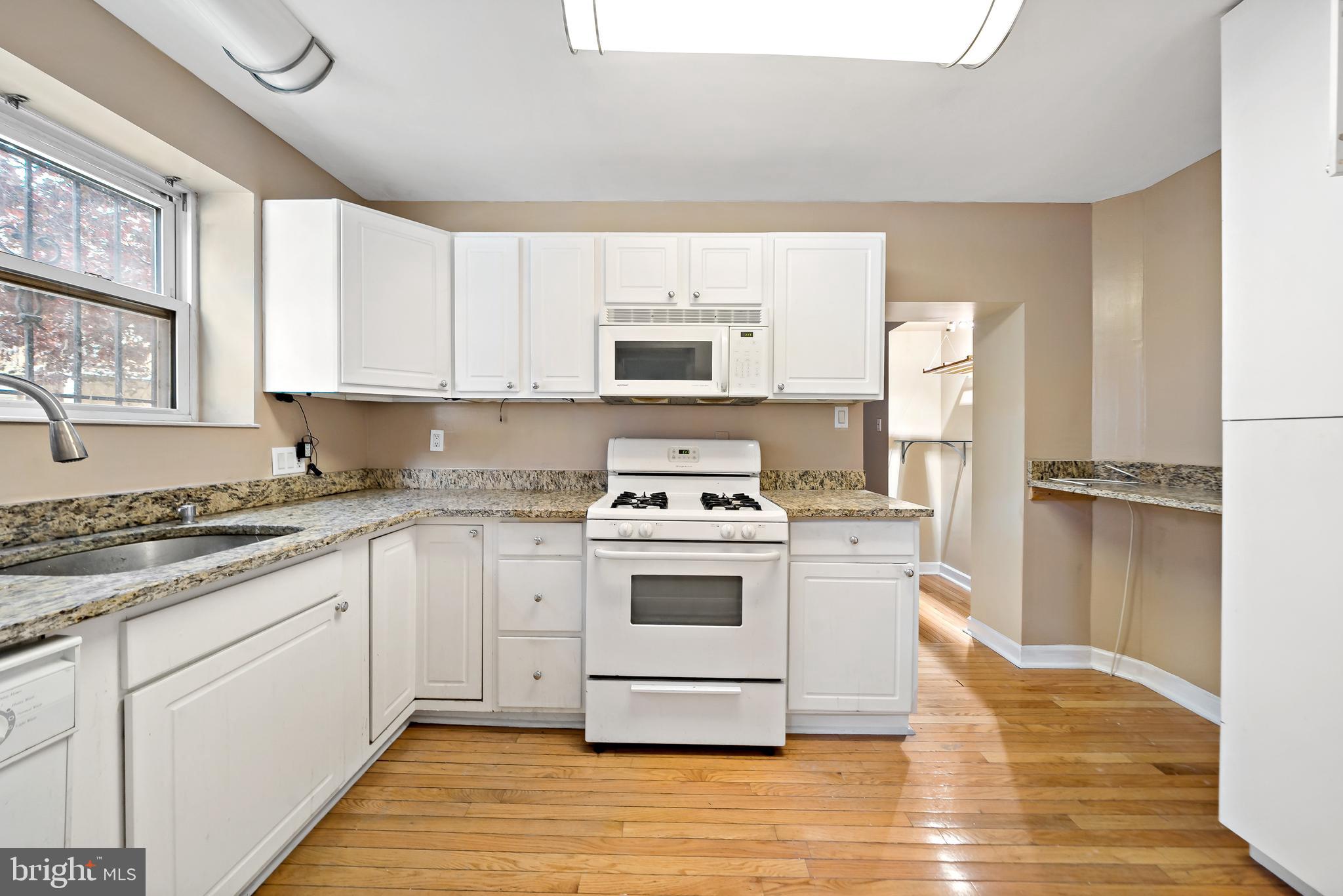 926 East Passyunk Avenue, Unit 1 Philadelphia, PA 19147 - Photo 2 of 19 a white kitchen with granite countertop a stove top oven microwave and cabinets
