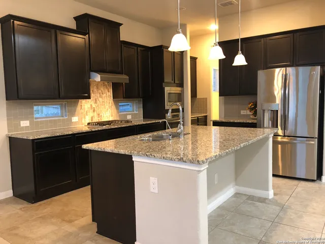 a kitchen with stainless steel appliances kitchen island granite countertop a sink refrigerator and cabinets