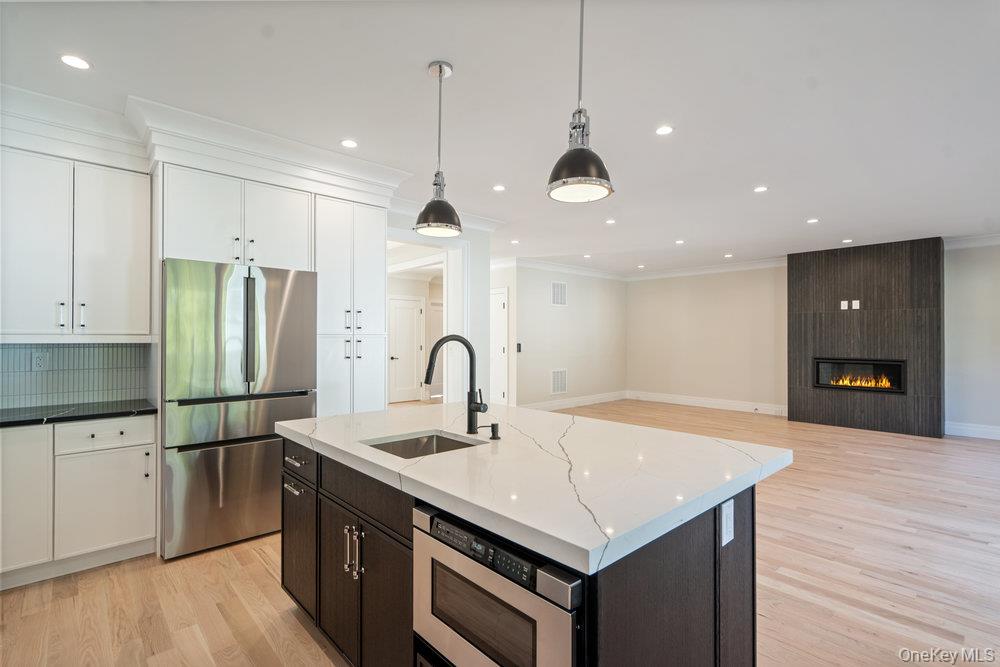 47 Netz Place Albertson, NY 11507 - Photo 38 of 41 Kitchen with appliances with stainless steel finishes, open floor plan, light wood-style flooring, a kitchen island with sink, and hanging light fixtures