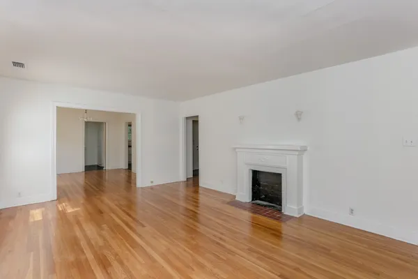 a view of an empty room with wooden floor fireplace and a window