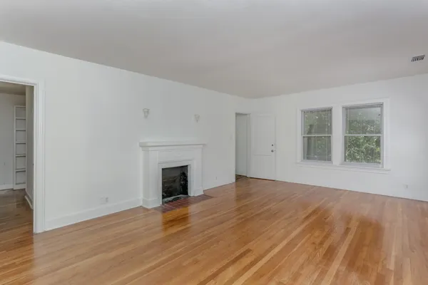 an empty room with wooden floor fireplace and windows