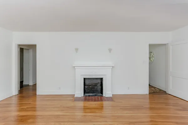 a view of an empty room with wooden floor and a fireplace