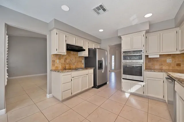 a kitchen with stainless steel appliances granite countertop a refrigerator oven a sink and white cabinets
