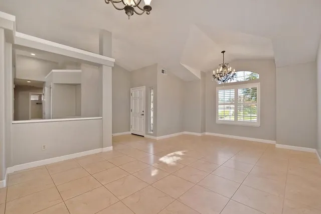 a view of an empty room with window and chandelier fan