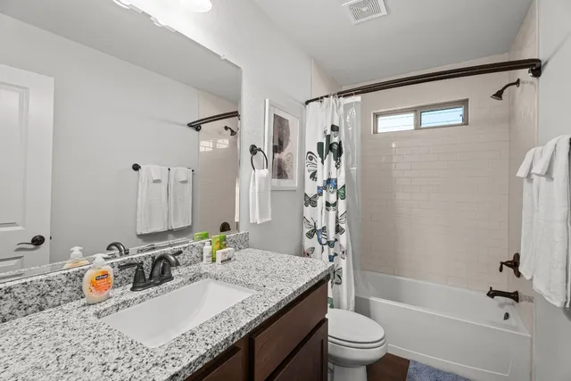 a bathroom with a granite countertop sink a toilet a mirror a vanity and shower