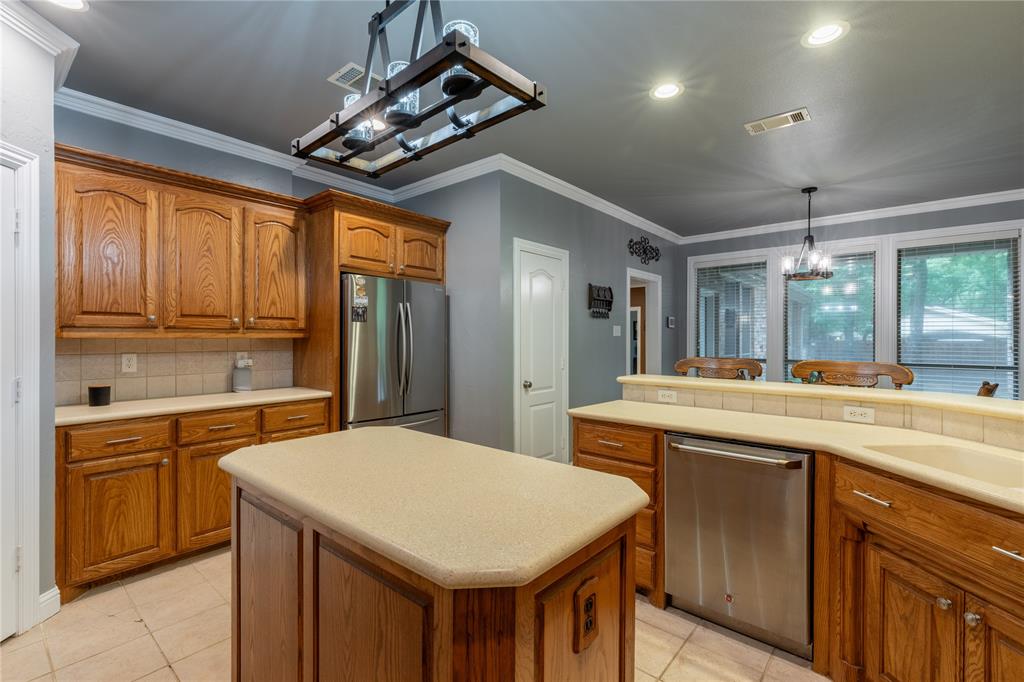 320 Rustic Oaks Road Combine, TX 75159 - Photo 14 of 40 Kitchen featuring appliances with stainless steel finishes, brown cabinetry, a chandelier, light countertops, and ornamental molding