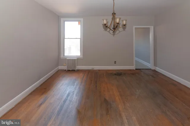 an empty room with wooden floor chandelier and windows