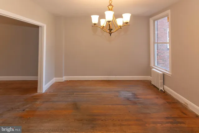 an empty room with wooden floor chandelier and windows