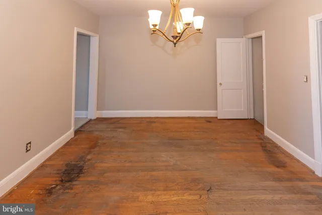an empty room with a chandelier fan and wooden floor