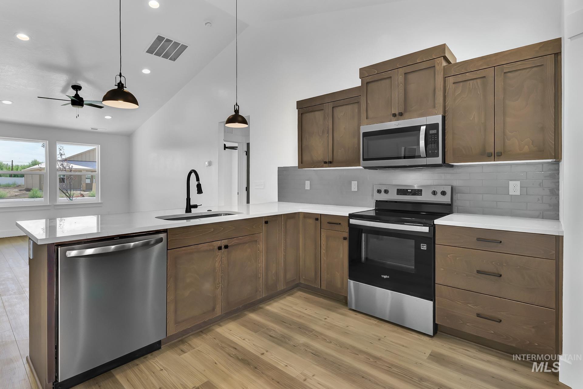 1160 Velvet Loop Wilder, ID 83676 - Photo 7 of 29 Kitchen with appliances with stainless steel finishes, backsplash, light wood-style floors, hanging light fixtures, and a peninsula