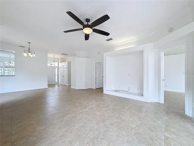 an empty room with a chandelier fan and windows