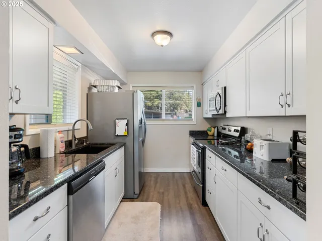 a kitchen with granite countertop a sink cabinets wooden floor and stainless steel appliances