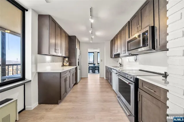 a kitchen with stainless steel appliances kitchen island granite countertop a refrigerator a stove a sink and a oven with wooden floor