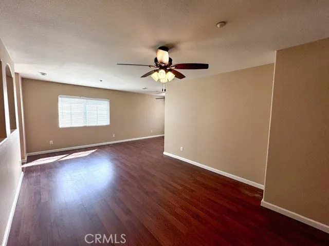 a view of an empty room with wooden floor and a ceiling fan