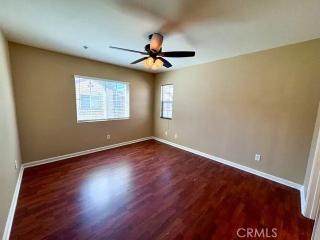 an empty room with wooden floor chandelier fan and windows