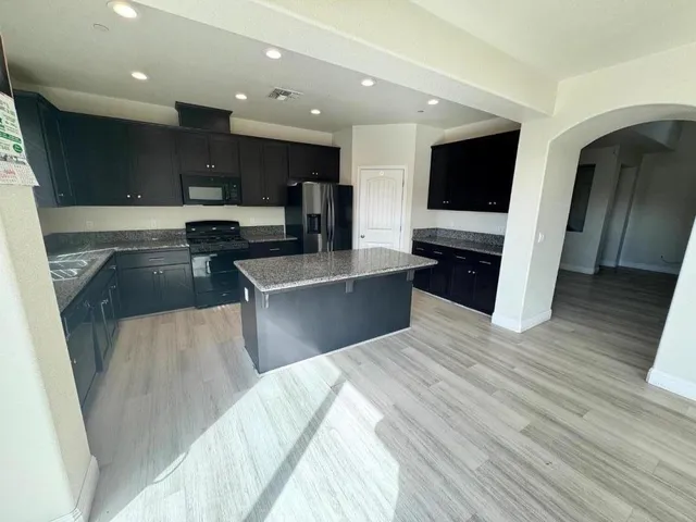 a large kitchen with stainless steel appliances kitchen island granite countertop a refrigerator and a stove top oven