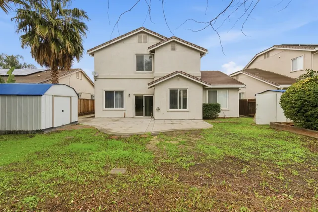 a view of a yard in front of a white house with plants and large tree