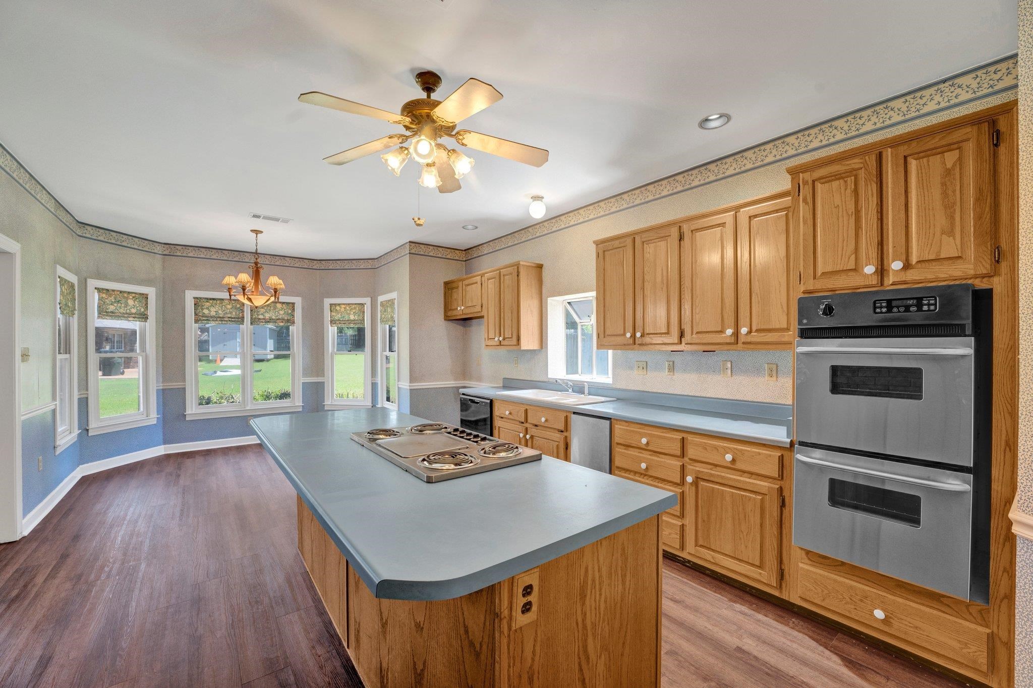 4149 Old Forest Road Memphis, TN 38125 - Photo 19 of 32 Kitchen featuring ceiling fan with notable chandelier, hanging light fixtures, a center island, wood-type flooring, and appliances with stainless steel finishes