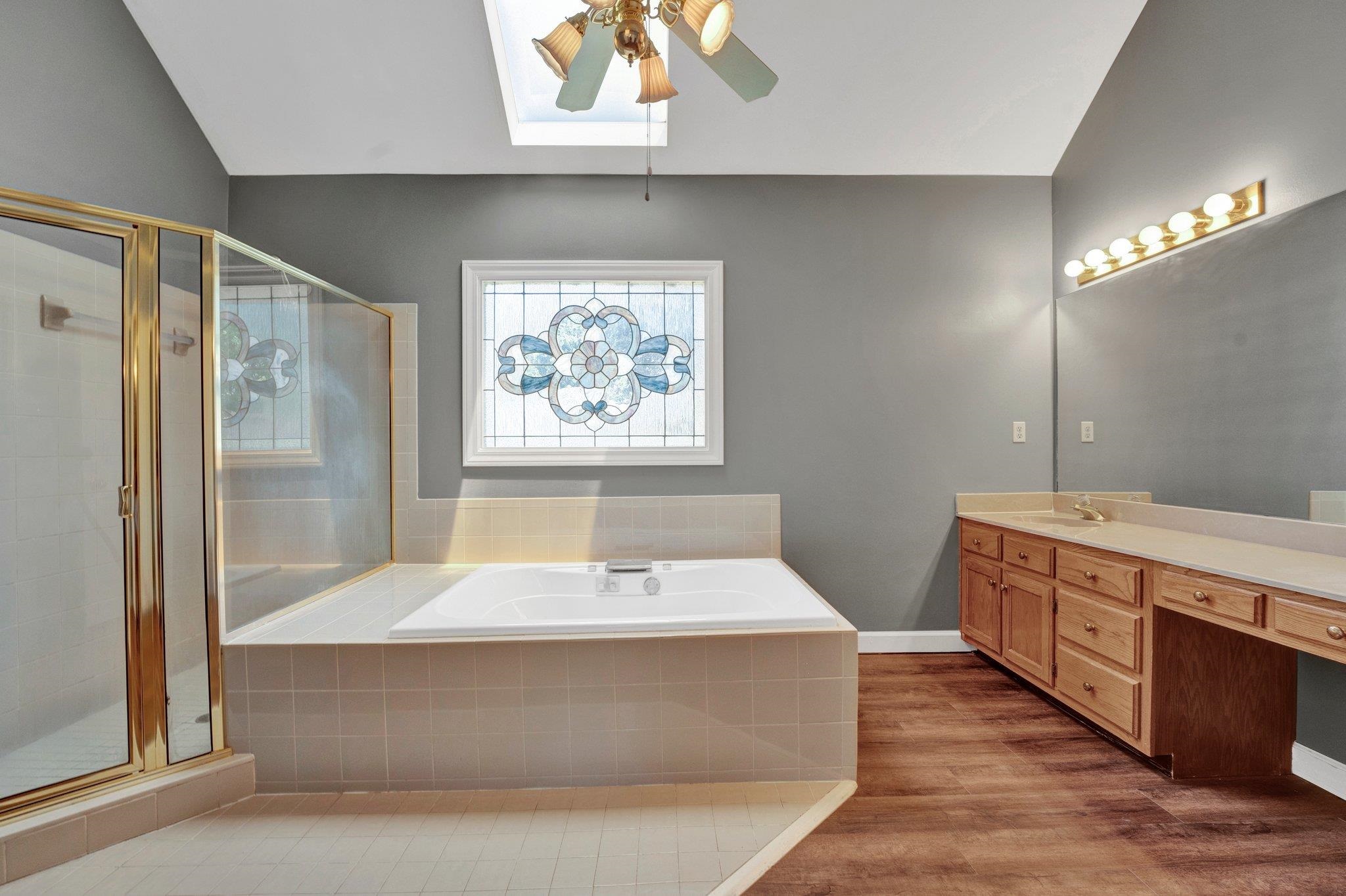 4149 Old Forest Road Memphis, TN 38125 - Photo 29 of 32 Bathroom with plus walk in shower, ceiling fan, wood-type flooring, lofted ceiling with skylight, and vanity