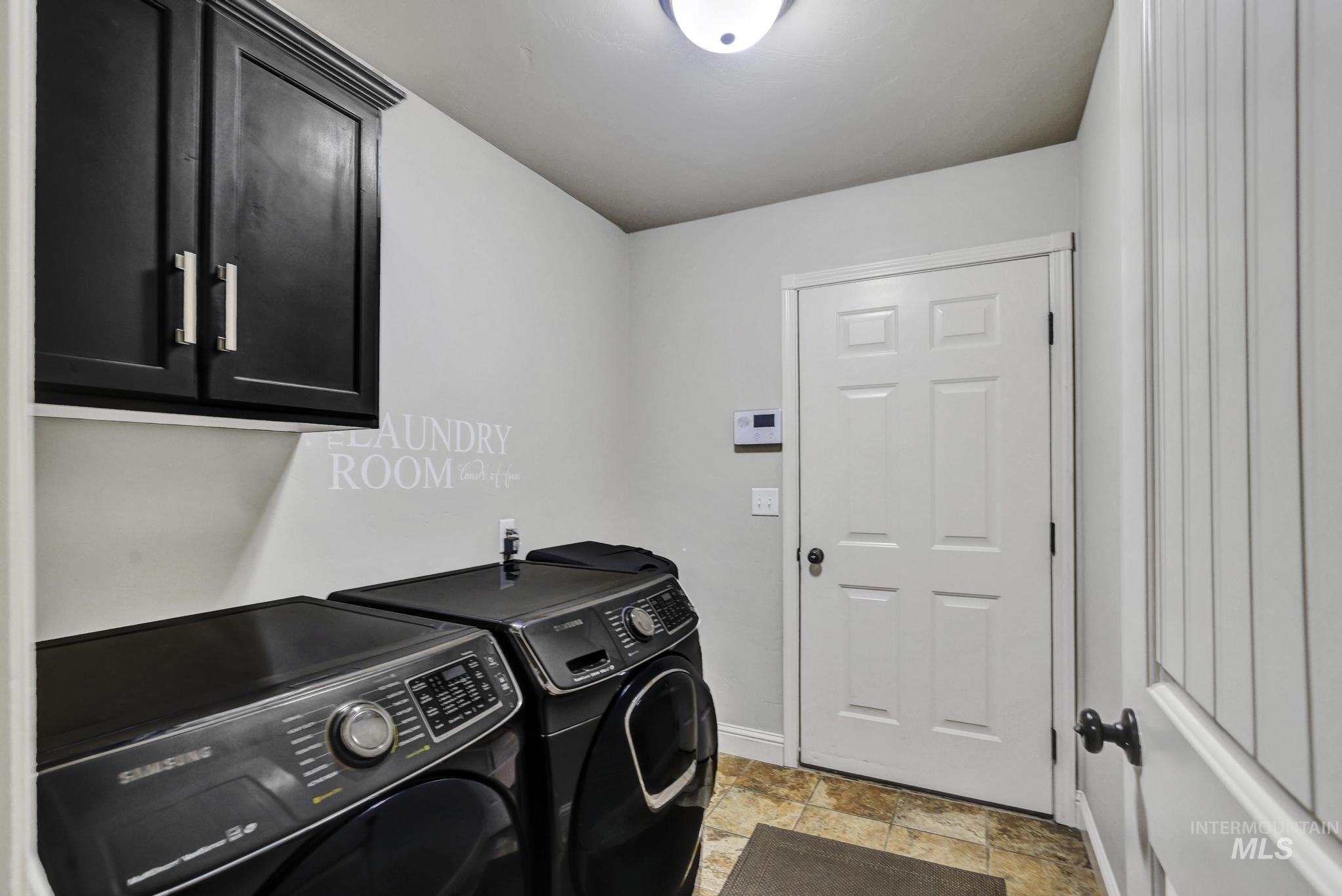 446 Noble Street Twin Falls, ID 83301 - Photo 24 of 42 Dedicated utility space featuring overhead black cabinetry with brushed nickel hardware, light-toned walls, a white six-panel door with a black doorknob, and patterned tile flooring