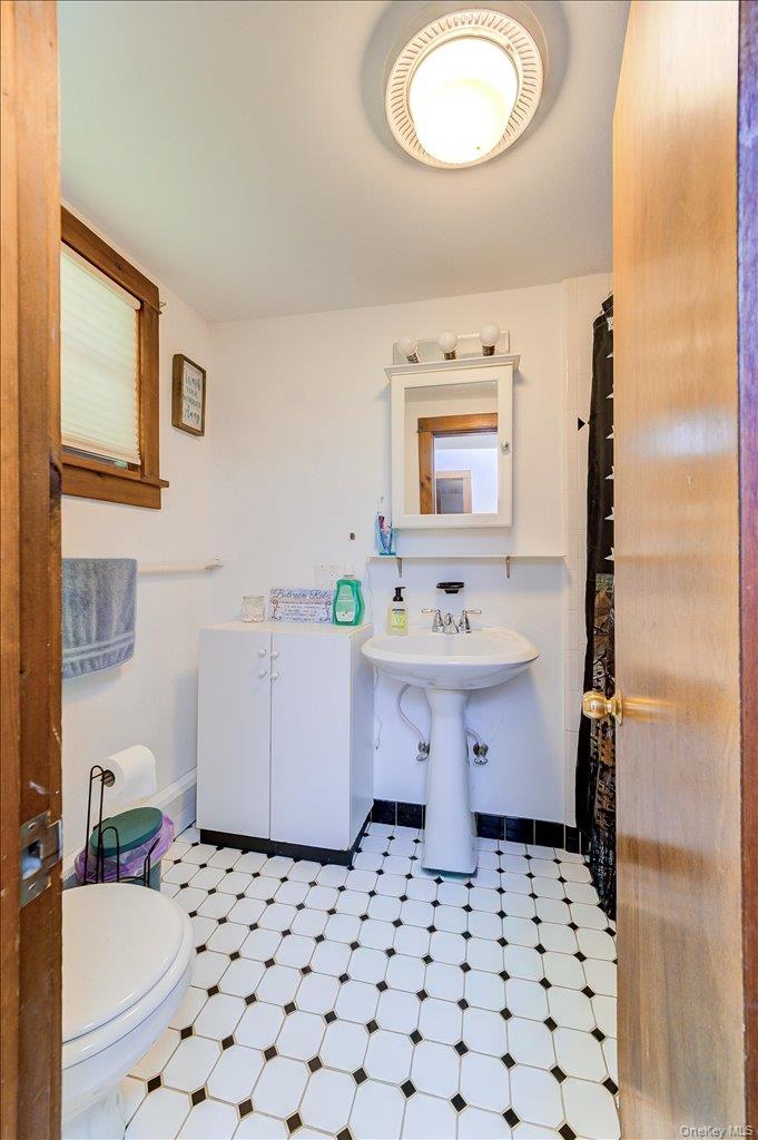 10-12 Woodlea Road Salt Point, NY 12578 - Photo 15 of 48 Bathroom featuring a black and white tiled floor, a white pedestal sink, a white medicine cabinet, a white storage cabinet, and a window with blinds