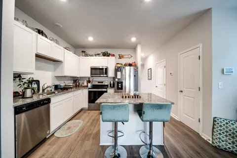 a kitchen with stainless steel appliances kitchen island granite countertop a refrigerator a stove a sink dishwasher and a dining table with wooden floor