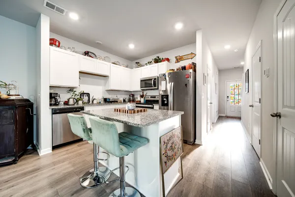 a kitchen with stainless steel appliances granite countertop a refrigerator a sink dishwasher a stove and a dining table with wooden floor