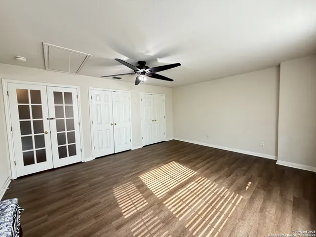 a view of an empty room with wooden floor and a ceiling fan