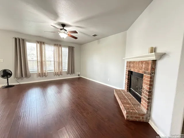 a view of an empty room with wooden floor fireplace and a window