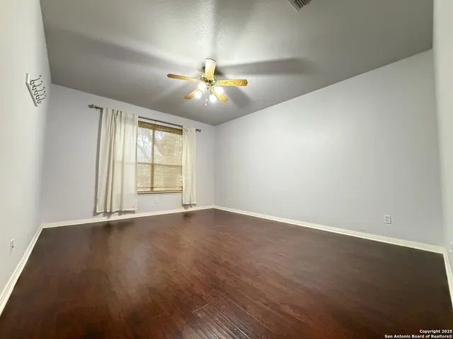 an empty room with wooden floor chandelier fan and windows