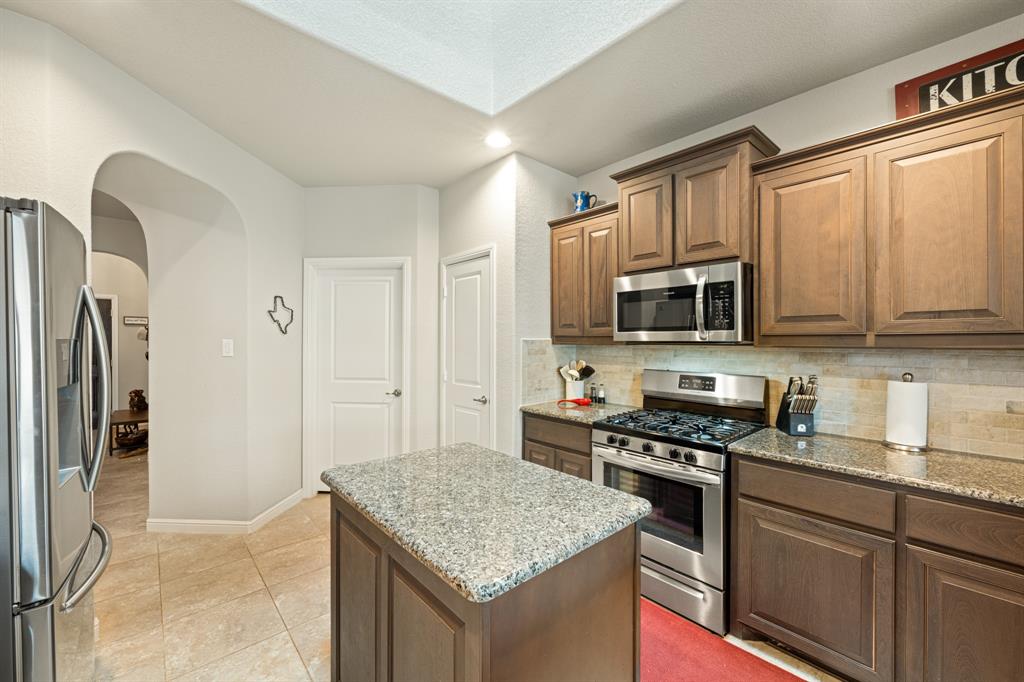 916 Falcon Road Argyle, TX 76226 - Photo 12 of 37 Kitchen featuring stainless steel appliances, light stone countertops, a center island, and decorative backsplash