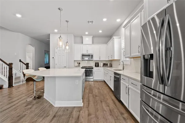 a kitchen with stainless steel appliances a refrigerator a sink dishwasher a stove and white cabinets with wooden floor