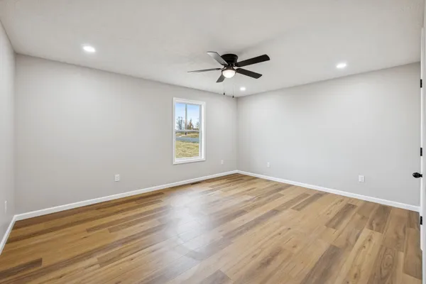 an empty room with wooden floor fan and windows