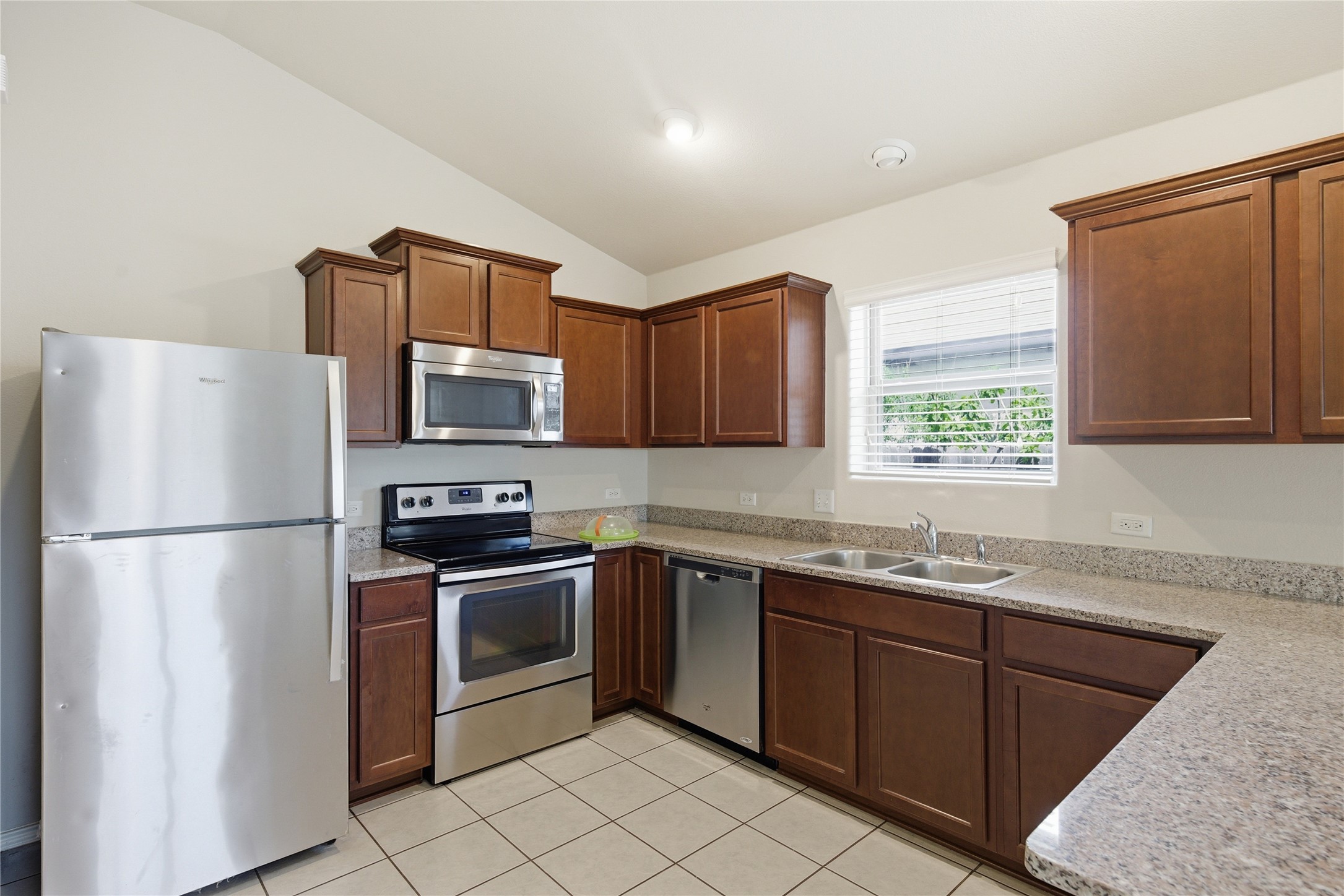 19325 Stokes Lane Pflugerville, TX 78660 - Photo 13 of 24 Kitchen with stainless steel appliances, lofted ceiling, light tile patterned flooring, and light stone counters