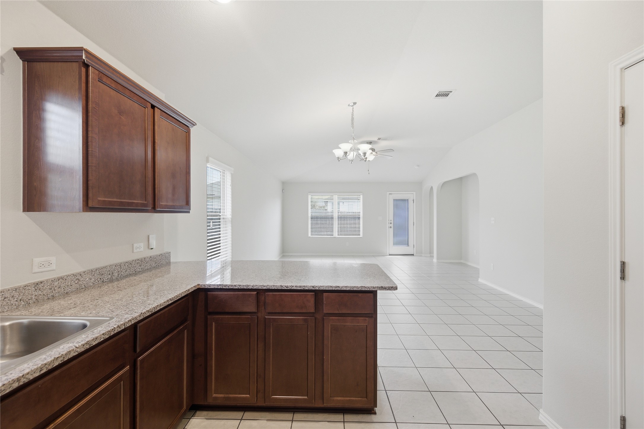 19325 Stokes Lane Pflugerville, TX 78660 - Photo 14 of 24 Kitchen with light tile patterned floors, a peninsula, dark wood finish cabinetry, arched walkways, and lofted ceiling