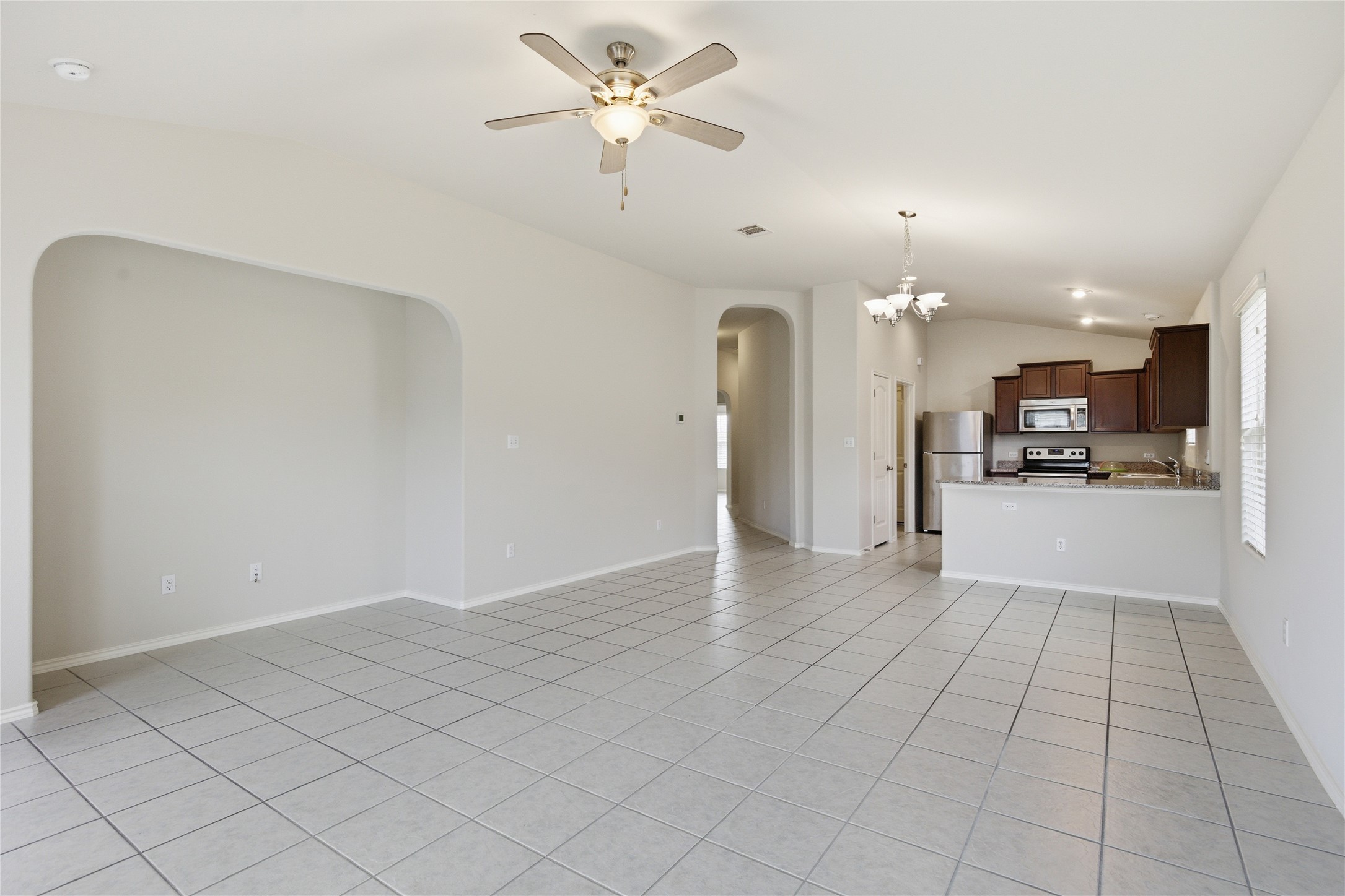 19325 Stokes Lane Pflugerville, TX 78660 - Photo 18 of 24 Unfurnished living room featuring vaulted ceiling, light tile patterned flooring, ceiling fan, a chandelier, and arched walkways