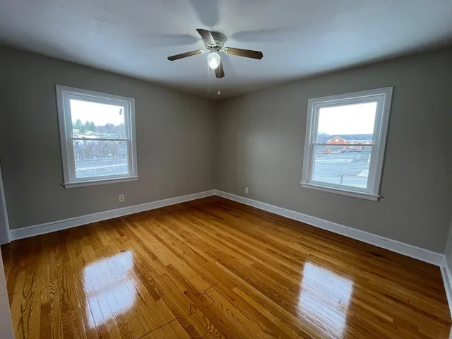 a view of an empty room with chandelier fan and wooden floor