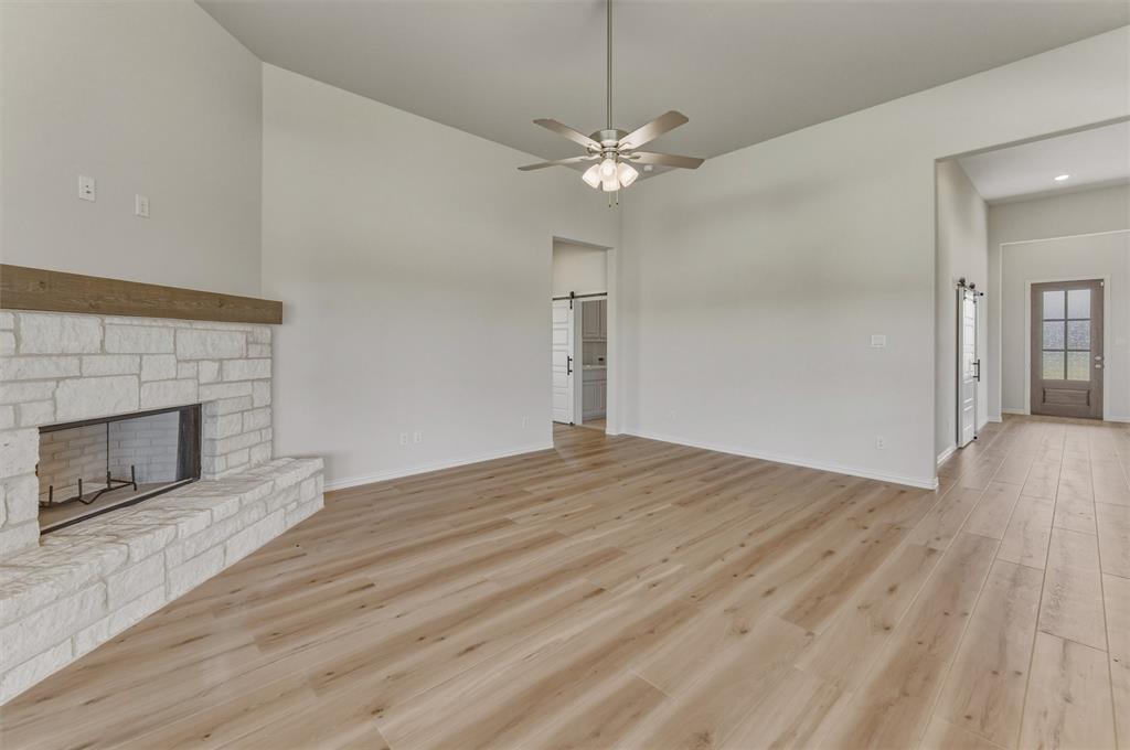 605 Tay Tay Way Springtown, TX 76082 - Photo 12 of 31 Spacious living area featuring light wood-finish flooring, a stone fireplace with a wood mantle, a ceiling fan, vaulted ceilings, and white interior walls