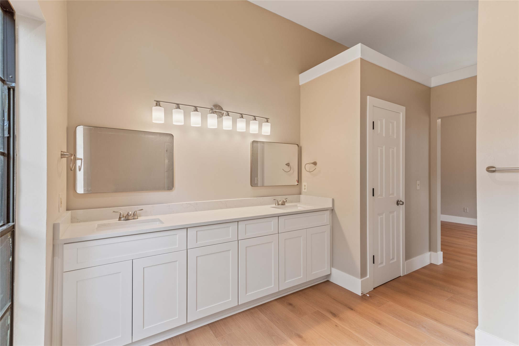 10 White Fawn Drive Spring, TX 77381 - Photo 22 of 25 This bathroom features a spacious double vanity with white cabinetry and modern fixtures. The room has warm beige walls, hardwood flooring, and ample lighting above the mirrors, creating a bright and inviting space.