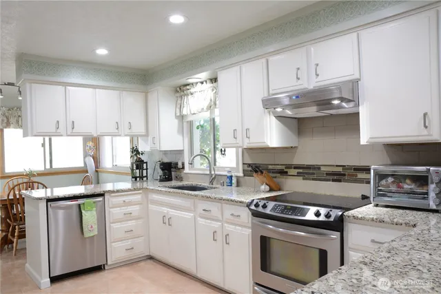 a kitchen with stainless steel appliances granite countertop a stove a sink and white cabinets