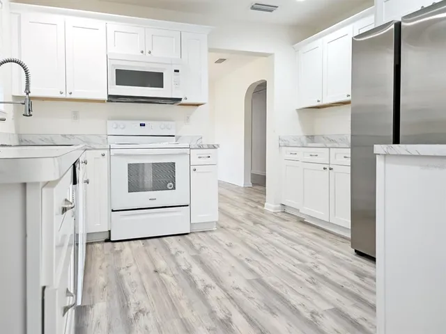 a kitchen with stainless steel appliances white cabinets a sink a stove a refrigerator and microwave with wooden floor