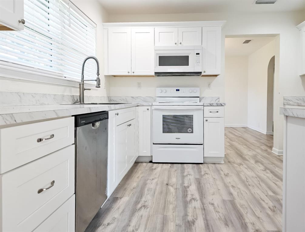 518 Northwest 27th Avenue Gainesville, FL 32609 - Photo 12 of 34 a kitchen with stainless steel appliances white cabinets a sink a stove a refrigerator and microwave with wooden floor