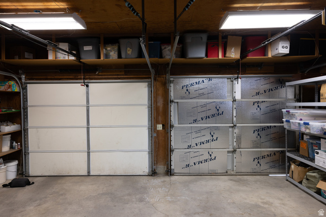 827 South 600 East Logan, UT 84321 - Photo 23 of 30 Two-car garage featuring a concrete floor, overhead fluorescent lighting, and accessible storage shelving