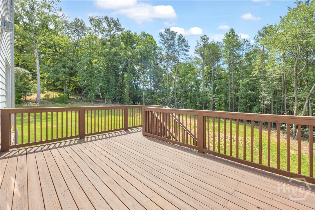 2476 St Martin Way Monroe, GA 30656 - Photo 65 of 75 Expansive elevated wood deck with a natural wood finish, featuring a full perimeter railing and a wooded backdrop