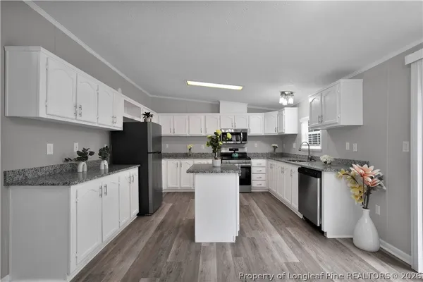 a kitchen with stainless steel appliances kitchen island granite countertop a stove top oven a sink a refrigerator and white cabinets with wooden floor
