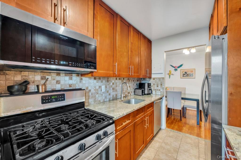 196-72 69th Avenue, Unit 1 Queens, NY 11365 - Photo 11 of 23 Kitchen featuring stainless steel appliances, light stone counters, brown cabinets, and decorative backsplash